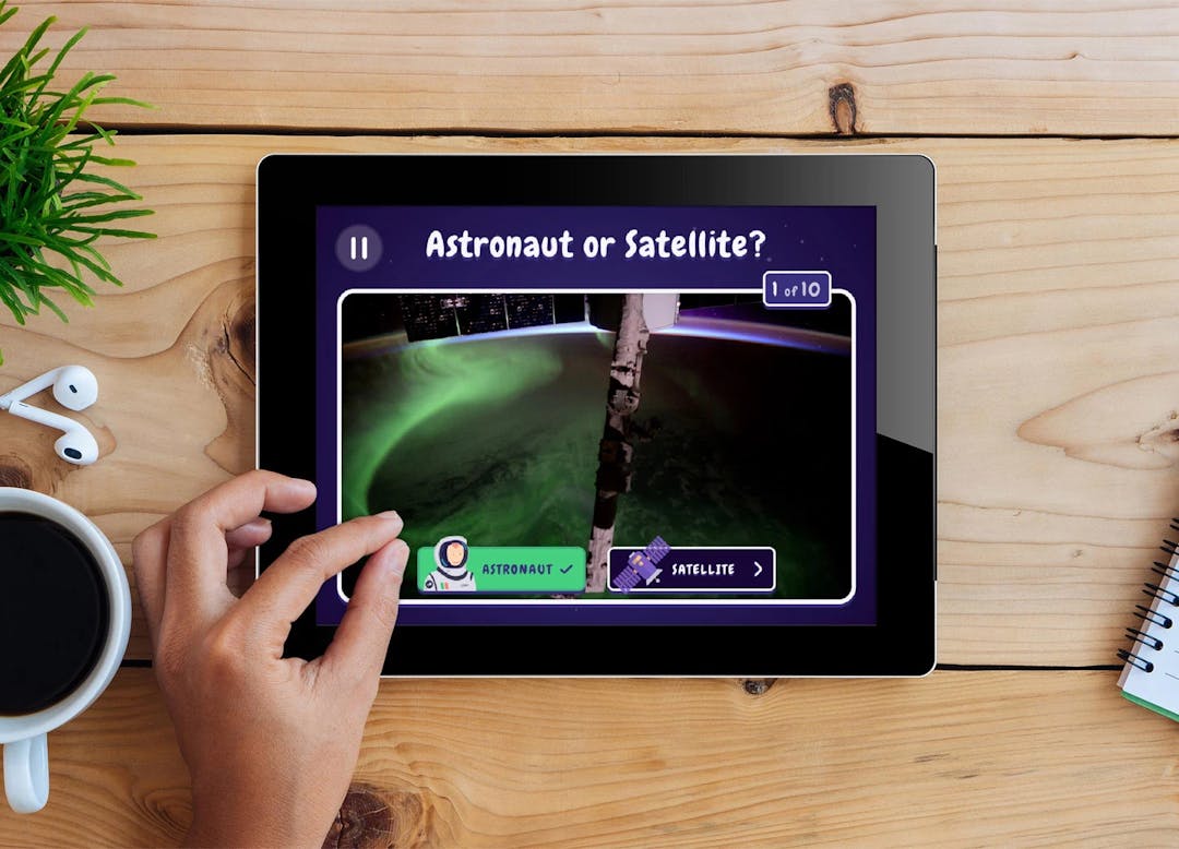 EO Detective app screen reading "Astronaut or Satellite?" on wooden table