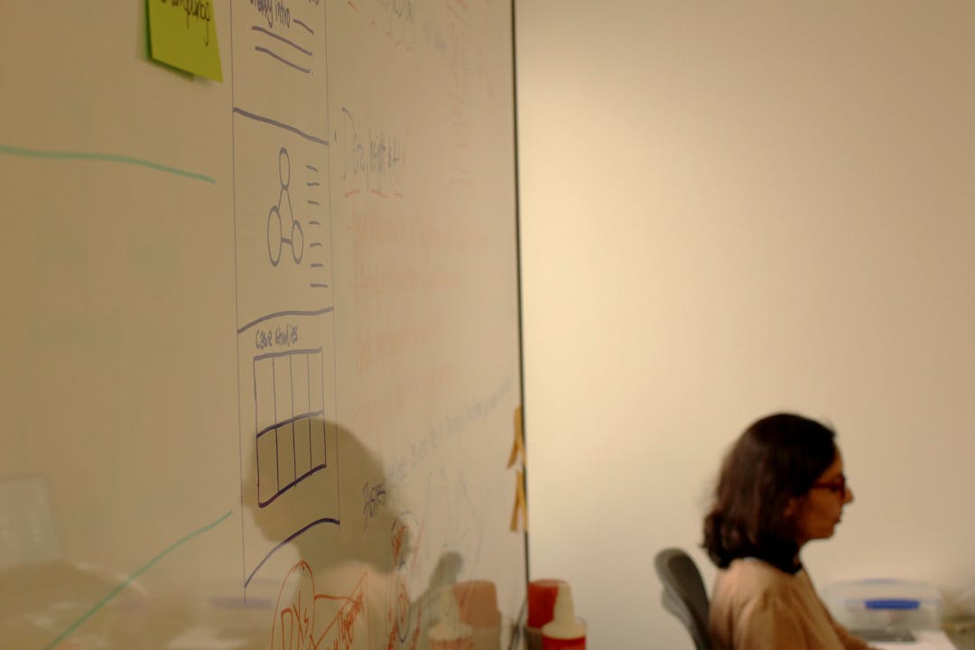 Digital Designer Kirti sat at desk, with mirrored image shown in whiteboard